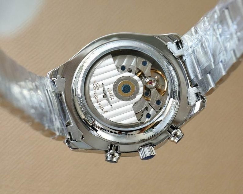 Op de afbeelding: Close-up van een zilverkleurig polshorloge met een transparante achterkant, waardoor de ingewikkelde interne werking van het horloge zichtbaar is. Het horloge heeft een zilveren band en een ronde wijzerplaat met de merknaam "Longines".