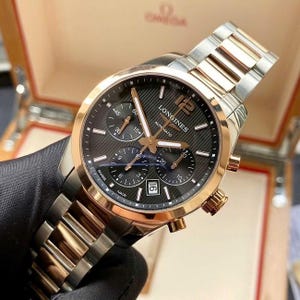 May include: A Longines automatic watch with a black dial, gold-tone hands and accents, and a date display. The watch features a stainless steel and gold-tone bracelet. The watch is in a box.