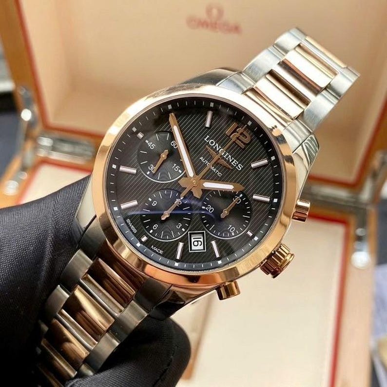 May include: A Longines automatic watch with a black dial, gold-tone hands and accents, and a date display. The watch features a stainless steel and gold-tone bracelet. The watch is in a box.