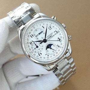 Op de afbeelding: Een zilverkleurig Longines automatisch horloge met een witte wijzerplaat, met meerdere subwijzerplaten voor datum en maanfase. Het horloge heeft een roestvrijstalen band en een gedetailleerde wijzerplaat met zwarte wijzers en cijfers. Het horloge is een luxe artikel.