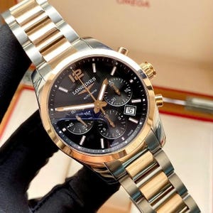 May include: A Longines automatic watch with a black dial, gold accents, and a stainless steel and gold-tone bracelet. The watch features chronograph subdials and a date window at the 3 o'clock position. The watch is Swiss made.