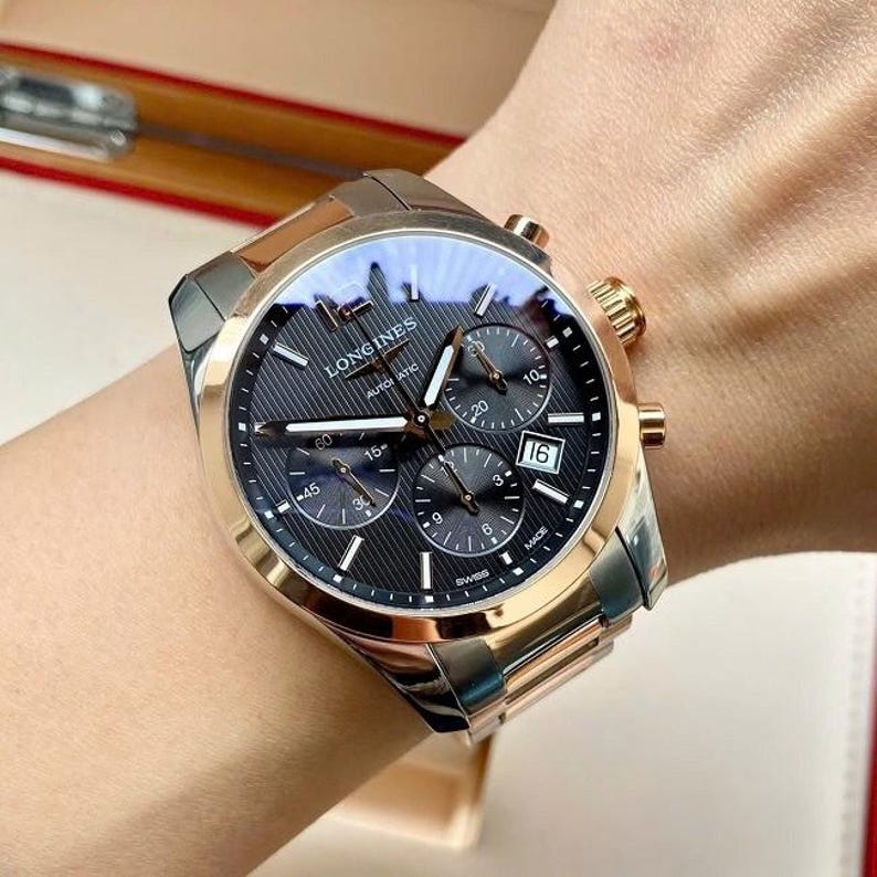 May include: A Longines automatic chronograph watch with a black dial, gold-tone accents, and a stainless steel and gold-tone bracelet. The watch features multiple sub-dials and a date display at the 3 o'clock position. The watch is Swiss made.