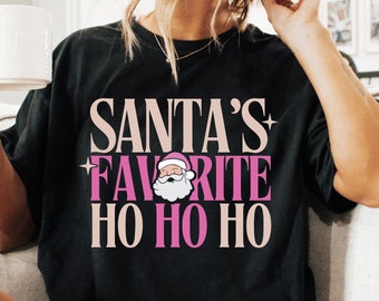 May include: A black t-shirt with the text "Santa's Favorite Ho Ho Ho" in pink and white lettering. A cartoon image of Santa Claus is included in the text.
