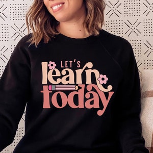 May include: Black sweatshirt with a pink and peach graphic that says "Let's learn today" with a pencil and flowers.