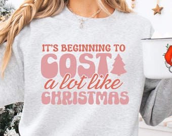 May include: A gray sweatshirt with a pink graphic that says "It's beginning to cost a lot like Christmas".