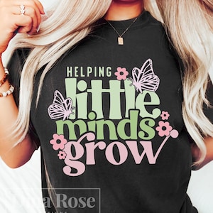 May include: Black t-shirt with the text "Helping little minds grow" in green and pink lettering. The text is surrounded by pink and green butterflies and flowers.