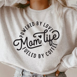 May include: A gray sweatshirt with a black circle graphic that says "Powered by Love, Mom Life, Fueled by Coffee".