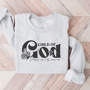 May include: A gray sweatshirt with a black graphic design that says "Child of God" with a butterfly and the text "Jesus is my savior".