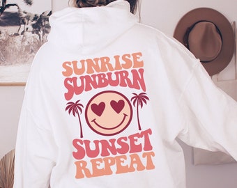 May include: White hoodie with a pink and orange graphic on the back that says "Sunrise Sunburn Sunset Repeat" with a smiley face with hearts for eyes and palm trees.