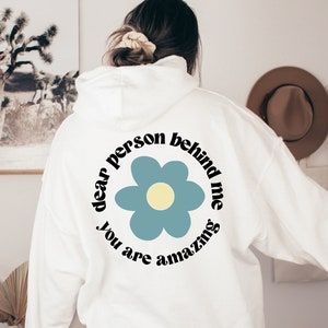 May include: White hoodie with a blue flower and the text "dear person behind me you are amazing" printed on the back.