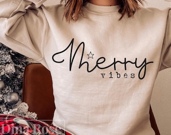 May include: A beige sweatshirt with the words "Merry vibes" in black script. The word "Merry" has a star above the "r". The word "vibes" is in a smaller font below "Merry". The person is wearing red and black plaid pants.