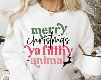 May include: White sweatshirt with the text "merry christmas ya filthy animal" in green, black, and pink. A black deer silhouette is included in the design. The sweatshirt is a festive holiday apparel item.