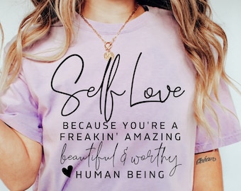 May include: A purple t-shirt with the text "Self Love because you're a freakin' amazing beautiful & worthy human being" in black lettering.