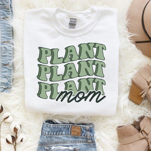 May include: White sweatshirt with green text that reads "Plant Plant Plant Mom".