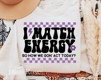 May include: White sweatshirt with a purple and black graphic that says "I Match Energy" with a lightning bolt and a flower. The text below the graphic says "So how we gon' act today?"