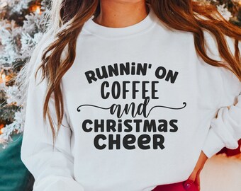 Op de afbeelding: Wit sweatshirt met zwarte tekst die "Runnin' on Coffee and Christmas Cheer" zegt.