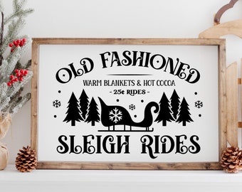 May include: A black and white sign with the text "Old Fashioned Warm Blankets & Hot Cocoa - 25¢ Rides - Sleigh Rides". The sign features a silhouette of a sleigh with a snowflake on top, pulled by a reindeer, and three pine trees.