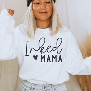 May include: White sweatshirt with black text that reads "Inked Mama" with a small black heart before the word "Mama".