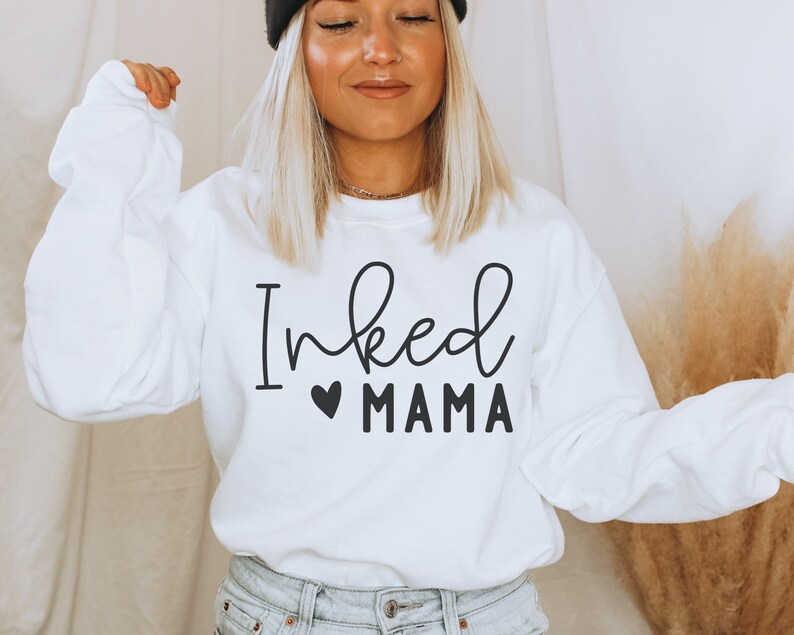 May include: White sweatshirt with black text that reads "Inked Mama" with a small black heart before the word "Mama".