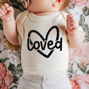 May include: A white baby onesie with a black heart and the word "loved" inside the heart.