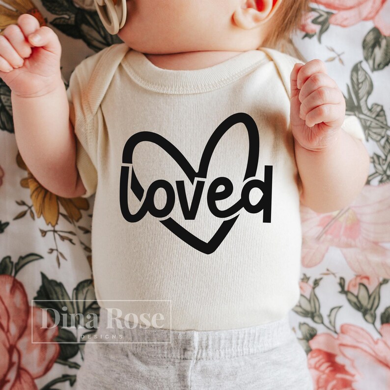 May include: A white baby onesie with a black heart and the word "loved" inside the heart.