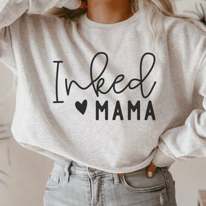 May include: A gray sweatshirt with the text "Inked Mama" in black lettering with a small heart symbol before the word "Mama".