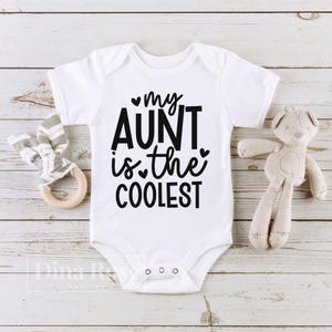 May include: White baby onesie with black text that reads "my aunt is the coolest" with a small heart symbol before "my" and "the".
