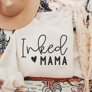 May include: A cream-colored sweatshirt with the text "Inked Mama" in black lettering with a small black heart between the words.