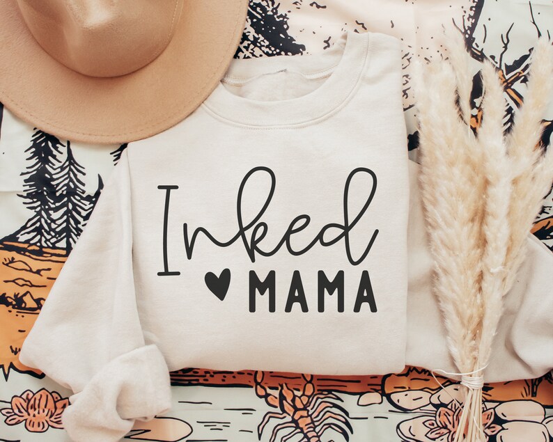 May include: A cream-colored sweatshirt with the text "Inked Mama" in black lettering with a small black heart between the words.