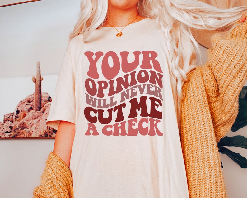 May include: A white t-shirt with the text "YOUR OPINION WILL NEVER CUT ME A CHECK" in a retro, colorful font.