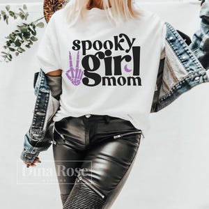 May include: White t-shirt with the text "spooky girl mom" in black with a purple skeleton hand and crescent moon graphic.