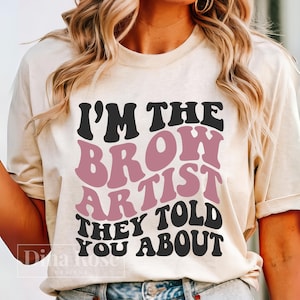 May include: A white t-shirt with the text "I'm the Brow Artist They Told You About" in black and pink retro-style lettering.