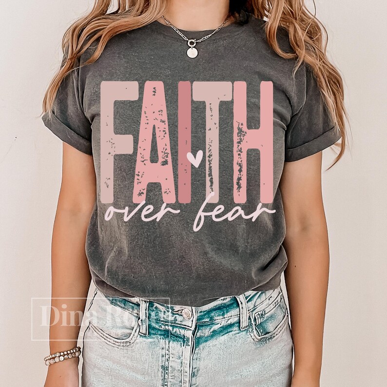 May include: Dark gray t-shirt with the words "FAITH over fear" in pink and white lettering. The word "FAITH" is in a bold, blocky font, and the word "fear" is in a cursive font. A small heart is between the words.