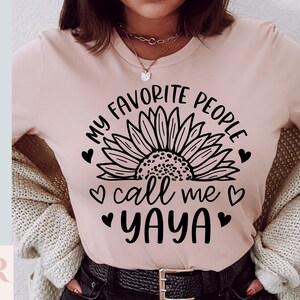 K&ouml;nnte beinhalten: Ein pinkfarbenes T-Shirt mit einer schwarzen Sonnenblumengrafik und dem Text "Meine Lieblingsmenschen nennen mich Yaya" mit Herzen um den Text.