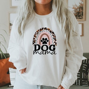 May include: White sweatshirt with a rainbow design featuring a paw print and the text "DOG mama". The rainbow is decorated with a leopard print pattern.