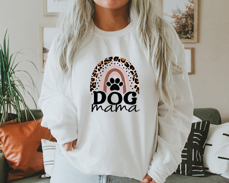 May include: White sweatshirt with a rainbow design featuring a paw print and the text "DOG mama". The rainbow is decorated with a leopard print pattern.