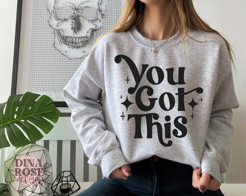 Puede incluir: Una sudadera gris con el texto "You Got This" en negro, en letras estilizadas. El texto est&aacute; rodeado de peque&ntilde;os signos m&aacute;s y diamantes.