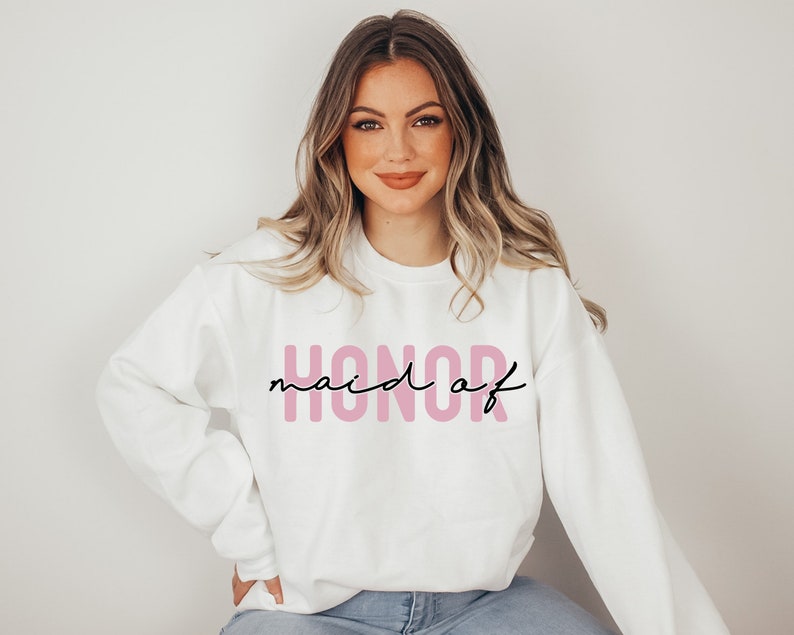 May include: White sweatshirt with the text "maid of honor" in pink letters and black script.