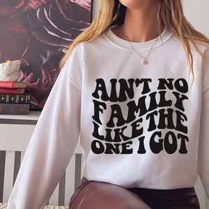 Pu&ograve; includere: Felpa bianca con testo nero che recita "Ain't no family like the one I got" in un font retr&ograve;.