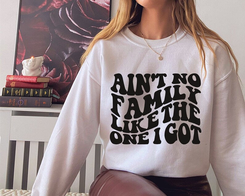 Pu&ograve; includere: Felpa bianca con testo nero che recita "Ain't no family like the one I got" in un font retr&ograve;.