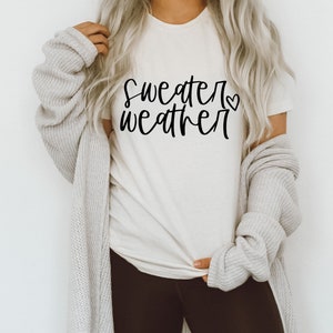 Puede incluir: Una camiseta blanca con el texto "sweater weather" en escritura negra con un peque&ntilde;o s&iacute;mbolo de coraz&oacute;n.