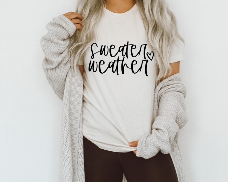 Puede incluir: Una camiseta blanca con el texto "sweater weather" en escritura negra con un peque&ntilde;o s&iacute;mbolo de coraz&oacute;n.