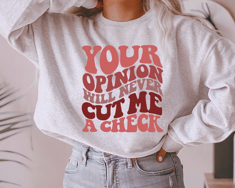 May include: A gray sweatshirt with the text "YOUR OPINION WILL NEVER CUT ME A CHECK" in a retro, colorful font.