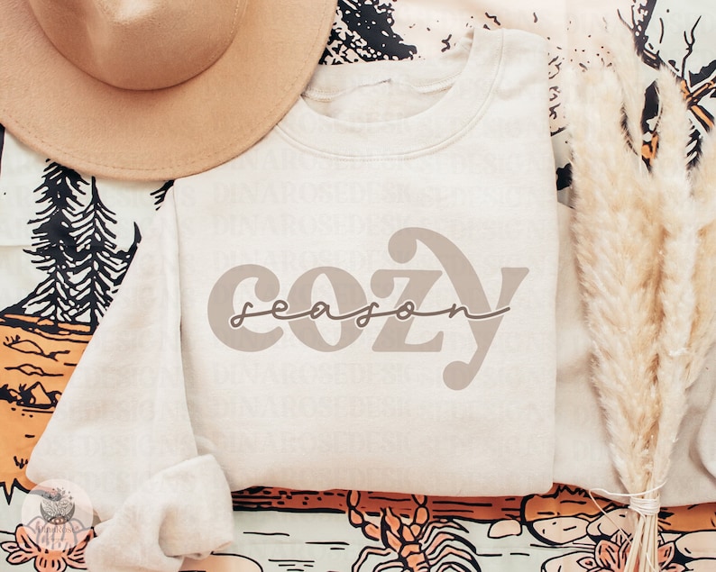 May include: A beige sweatshirt with the text "cozy season" in a brown font.