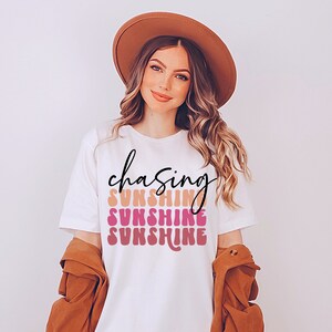 May include: White t-shirt with the text "chasing sunshine" in black script and the word "sunshine" repeated three times in a colorful, retro font.
