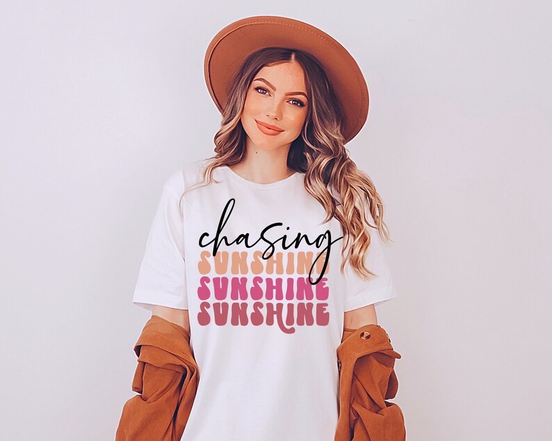 May include: White t-shirt with the text "chasing sunshine" in black script and the word "sunshine" repeated three times in a colorful, retro font.