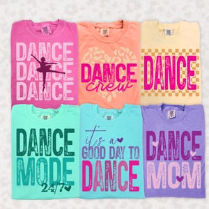 Peut inclure: Six t-shirts colorés avec des graphiques sur le thème de la danse. Les chemises sont dans des tons de rose, pêche, jaune, sarcelle, bleu clair et violet. Chaque chemise présente le mot "DANCE" en lettres grasses, ainsi que d'autres phrases et images liées à la danse.