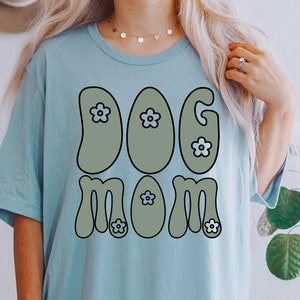 May include: A light blue t-shirt with a retro-style graphic that says "DOG MOM" in green letters with blue flowers.