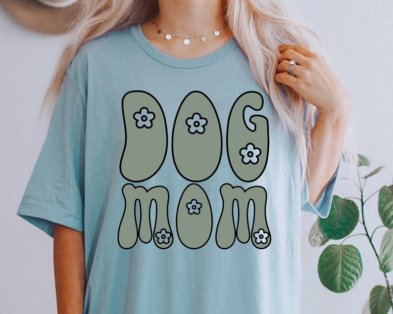 May include: A light blue t-shirt with a retro-style graphic that says "DOG MOM" in green letters with blue flowers.