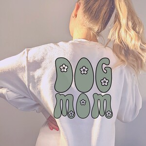 May include: White sweatshirt with a green "DOG MOM" graphic with white flowers on the back.